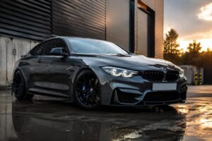 Dark grey factory-modified performance car with subtle styling upgrades, black alloy wheels and lowered suspension outside a modern industrial building.