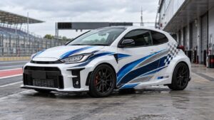 White Toyota GR Yaris with blue and silver motorsport graphics parked in a pit lane