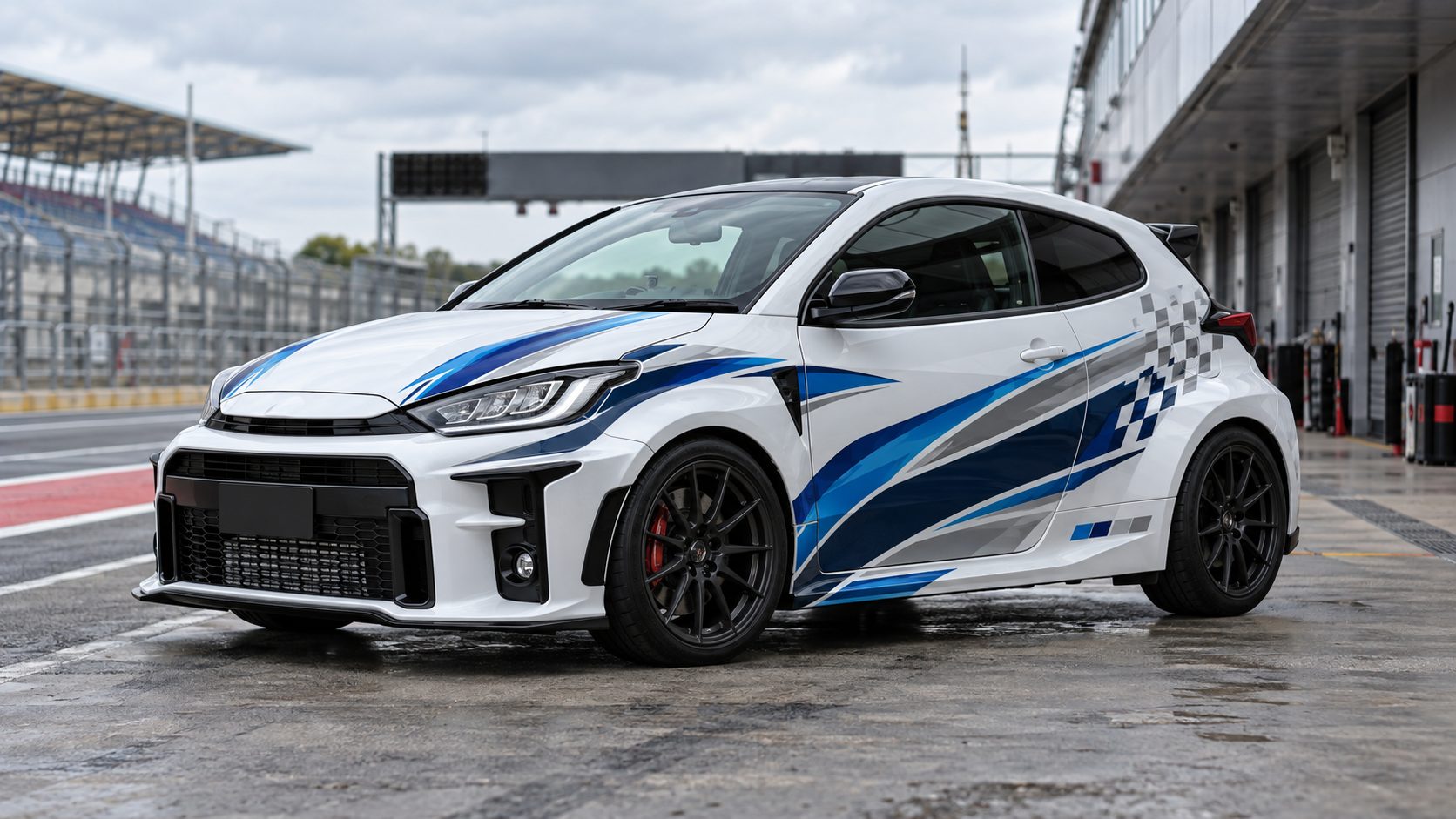 White Toyota GR Yaris with blue and silver motorsport graphics parked in a pit lane